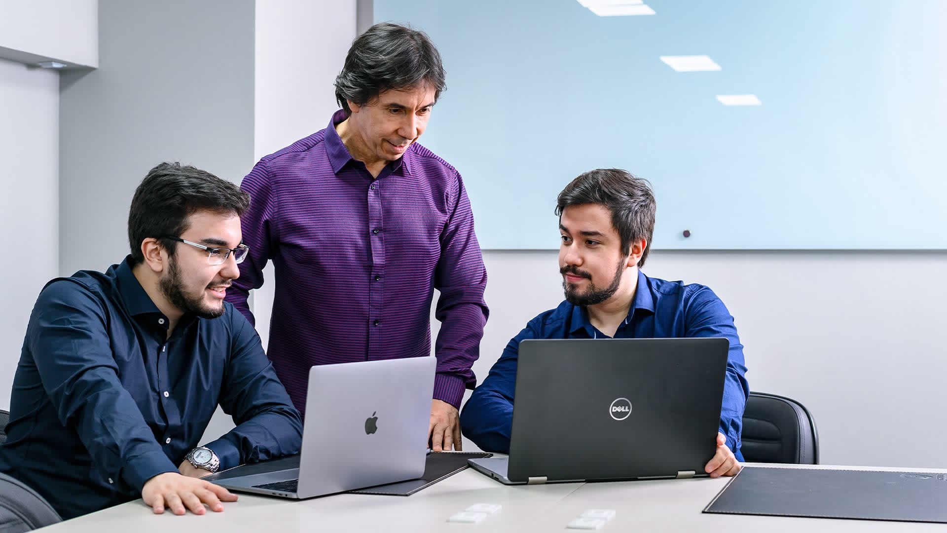 Imagem com 3 homens em frente a 2 notebooks
